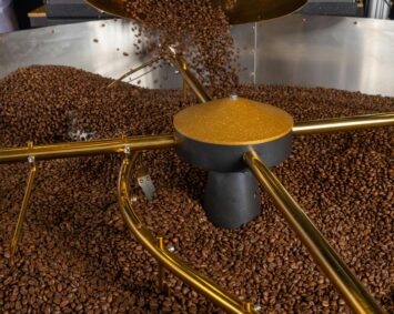 Freshly roasted coffee beans pouring into a cooling tray in an industrial factory setting.