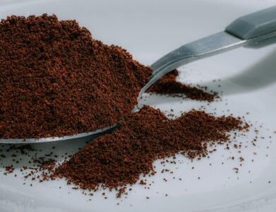 Closeup of aromatic fresh ground coffee powder heaped in silver teaspoon placed on white surface