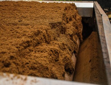 Detailed view of brown soil on an industrial conveyor belt inside a processing facility.