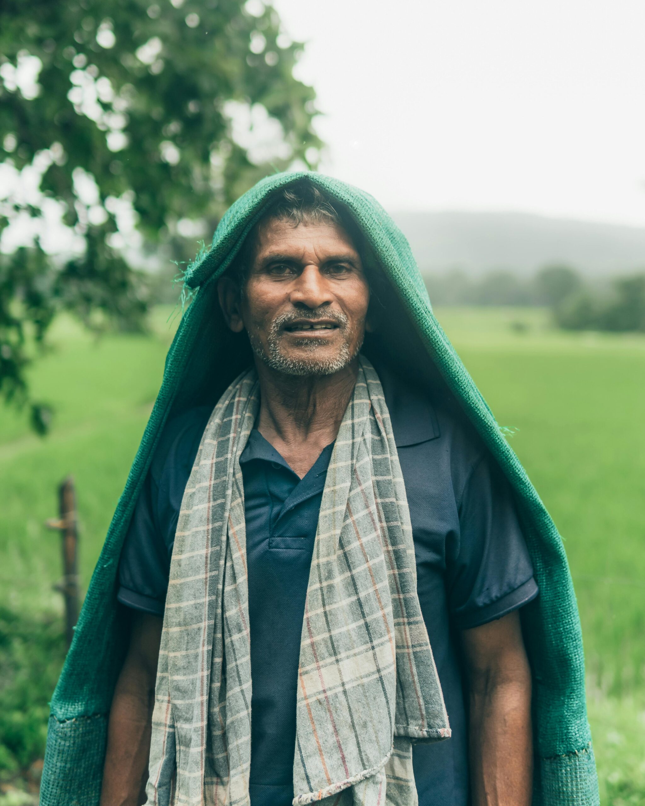 A farmer in GA, India, stands in a verdant field, draped in a cloth for rain protection.