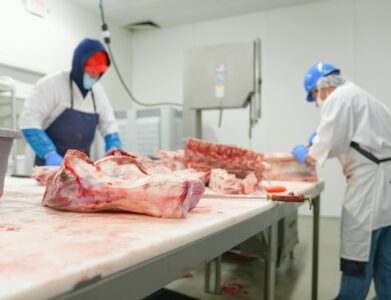 Two butchers process raw meat in an indoor industrial facility, highlighting freshness and safety.