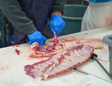 Close-up of a butcher processing meat with gloves on, highlighting food preparation techniques.