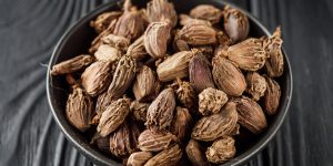 a barrel of dried black cardamom on a black wooden rustic background.