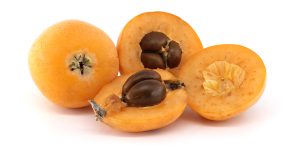 Delicious loquats, also known as Japanese plums, are shown whole and sliced, revealing their inner seeds. The fruits are set on a white backdrop.