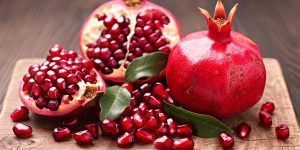 A closeup view of freshly cut pomegranates revealing their seeds on a wooden board with green leaves