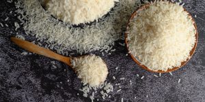 Milled rice in a bowl and a wooden spoon on the black cement floor. Top view