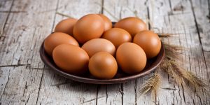 fresh brown eggs in plate and wheat ears on rustic wooden background