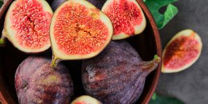 Fresh figs and fig halves on a brown old clay plate. Dark background, close-up top view. Seasonal ripe fruits, mediterranean diet