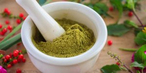 Fresh herbs powder in the mortar on wood background, alternative medicine
