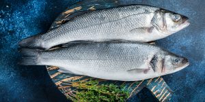 Uncooked Raw Sea Bass fish, Seabass with thyme. Blue background. Top view.